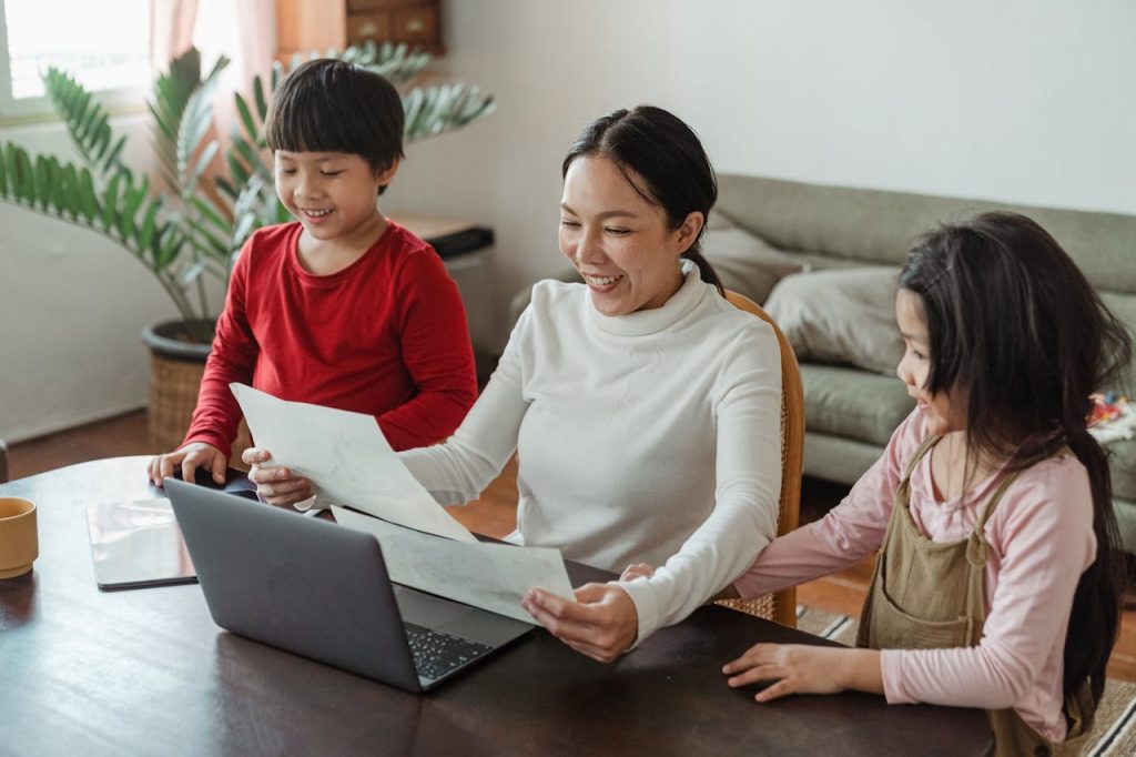 a mother working on a laptop with two kids beside her