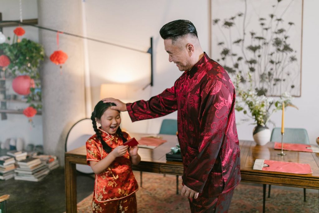 an asian father patting his young daughter's head, both wearing traditional chinese clothing