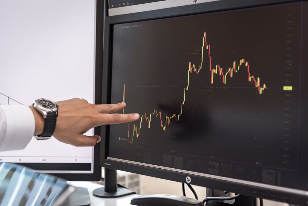 A hand pointing to a monitor screen displaying investment movements