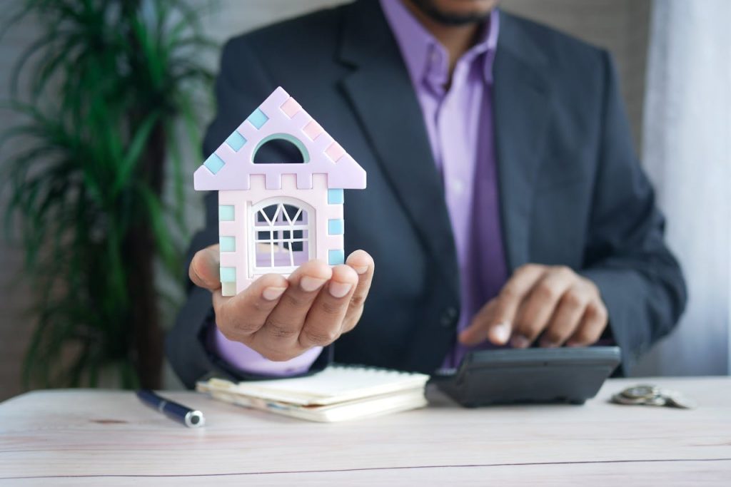 a person using a calculator while holding a small model house in his other hand