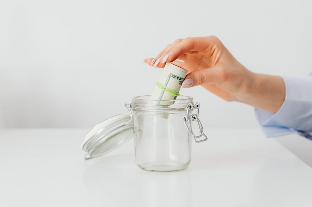 a hand putting rolled up dollar bills into a jar