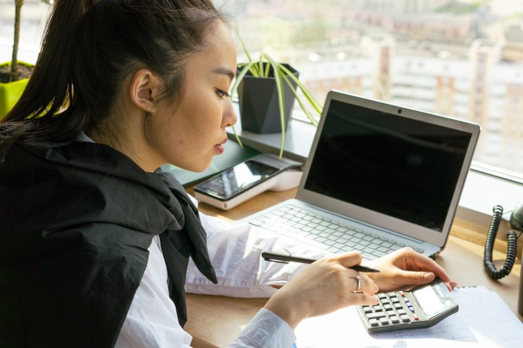 Woman Holding a Black Pen Using a Black Calculator