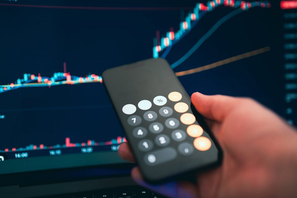 Close-up of a smartphone displaying a calculator with a financial chart in the background