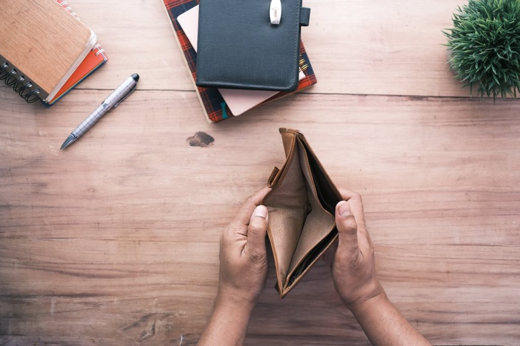 Top view of hands holding an open empty wallet on a wooden desk with notebooks and pen